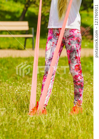 Girl doing exercises outdoor, using resistance fit band. 123760911