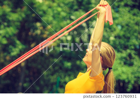 Girl doing exercise outdoor, using resistance fit band. 123760931