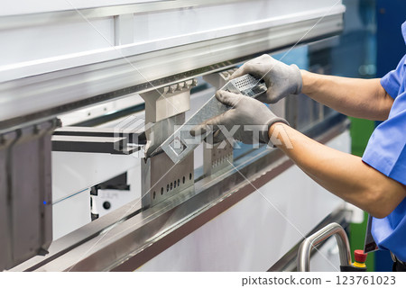 Close up the bending machine operator hold the sheet metal parts with rubber glove. Close up the bending machine operator hold the sheet metal parts with rubber glove. 123761023
