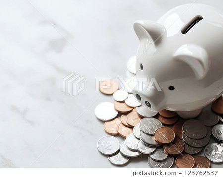 White ceramic piggy bank surrounded by scattered coins on a marble surface 123762537