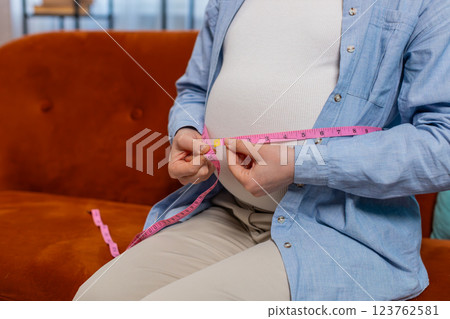 Pregnant woman measuring belly diameter with measure tape awaiting childbirth monitoring body change Pregnant woman measuring belly diameter with measure tape awaiting childbirth monitoring body change 123762581