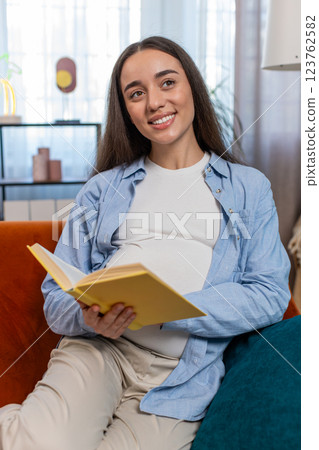 Pregnant Caucasian woman reading book advice child care guide feeling relax on cozy couch at home Pregnant Caucasian woman reading book advice child care guide feeling relax on cozy couch at home 123762582