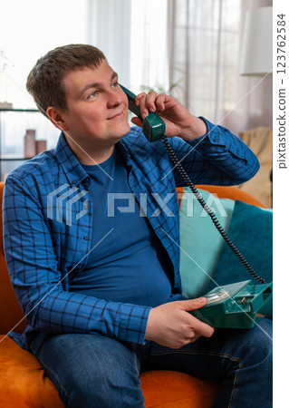 Man making old-fashioned retro telephone conversation talking with friends sitting on home sofa Man making old-fashioned retro telephone conversation talking with friends sitting on home sofa 123762584
