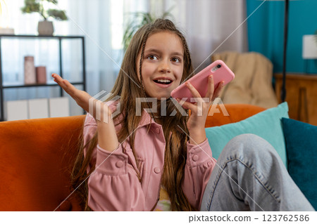 Happy girl child making online phone call conversation loudspeaker talking with friends at home Happy girl child making online phone call conversation loudspeaker talking with friends at home 123762586