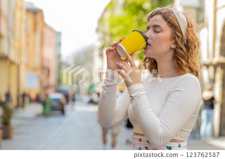 Happy redhead young smiling woman relaxing enjoying morning coffee hot drink outdoors city street Happy redhead young smiling woman relaxing enjoying morning coffee hot drink outdoors city street 123762587