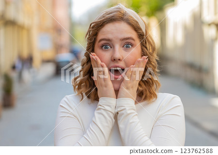 Redhead woman looking surprised at camera shocked by sudden win good victory news wow in city street Redhead woman looking surprised at camera shocked by sudden win good victory news wow in city street 123762588