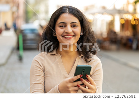 Indian woman use smartphone typing text messages browsing internet finishing work looking at camera Indian woman use smartphone typing text messages browsing internet finishing work looking at camera 123762591