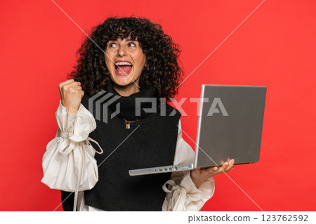 Excited happy young woman working on laptop winning online lottery game celebrating success victory Excited happy young woman working on laptop winning online lottery game celebrating success victory 123762592