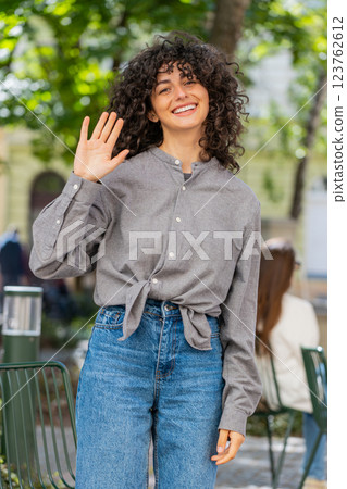 Young woman smiling friendly at camera, waving hands hello, hi, greeting or goodbye in city street Young woman smiling friendly at camera, waving hands hello, hi, greeting or goodbye in city street 123762612