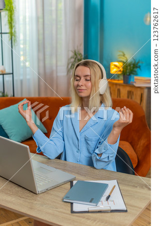 Young woman in headphones meditating doing yoga breathing exercise relaxing sitting at home office Young woman in headphones meditating doing yoga breathing exercise relaxing sitting at home office 123762617