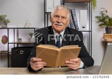 Bored Caucasian senior businessman reading book, literature, taking a rest after work at table Bored Caucasian senior businessman reading book, literature, taking a rest after work at table 123762648