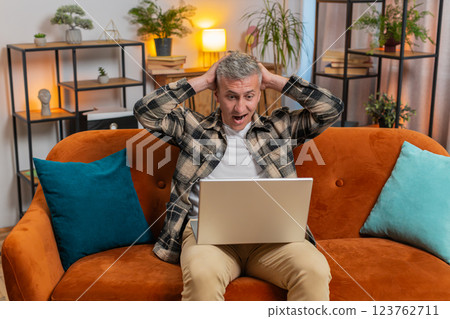 Amazed young man use laptop computer, receive good news message, shocked by victory, celebrate win 123762711