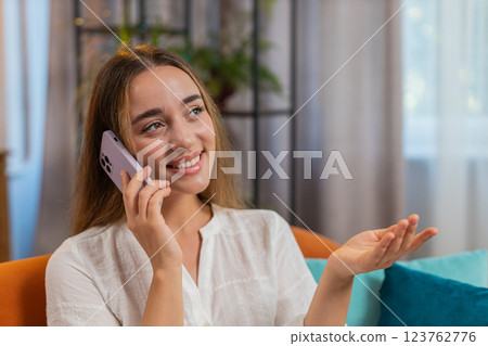 Happy young Caucasian woman making mobile phone conversation with friends sitting on couch at home Happy young Caucasian woman making mobile phone conversation with friends sitting on couch at home 123762776