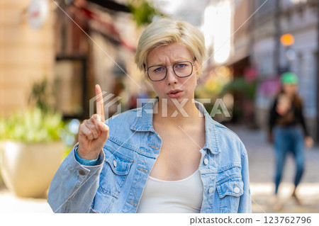 Upset young blonde woman reacting to unpleasant awful idea shaking finger at camera on city street Upset young blonde woman reacting to unpleasant awful idea shaking finger at camera on city street 123762796