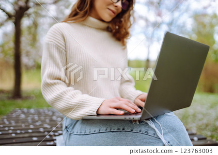 Close-up of woman's hand typing on laptop with notepad at table in park. Concept of remote work. Close-up of woman's hand typing on laptop with notepad at table in park. Concept of remote work. 123763003