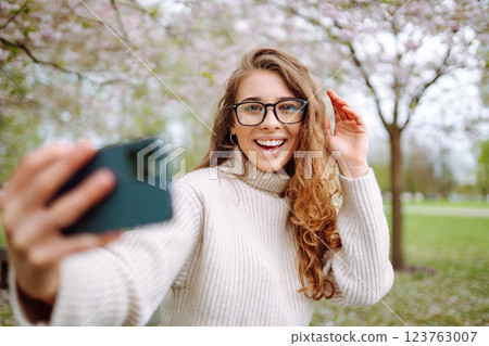 Selfie time. Young woman takes selfie photo in blooming spring park. Concept of relaxation, walking. Selfie time. Young woman takes selfie photo in blooming spring park. Concept of relaxation, walking. 123763007