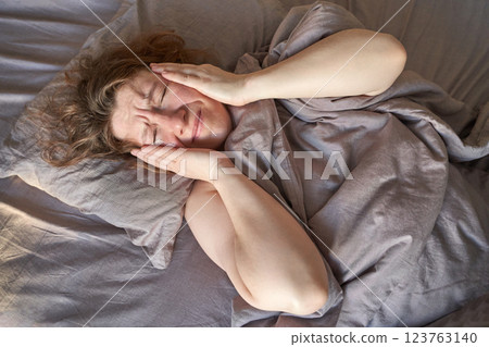 Caucasian adult female lying in bed with headache holding her head in painful Caucasian adult female lying in bed with headache holding her head in painful 123763140