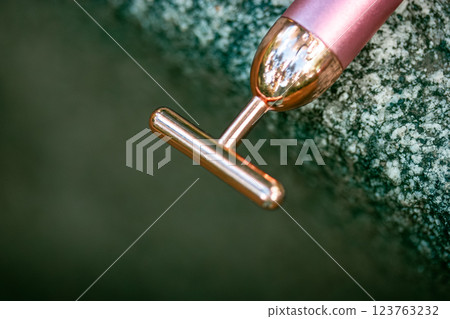 Golden T shape face massager with vibration on a grey granite podium top view. Female face beauty tool. Micro-vibrating roller massager. Daily routine 123763232