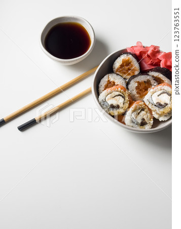Sushi rolls in a bowl with pink ginger and soy sauce and wooden sticks on white table top view 123763551