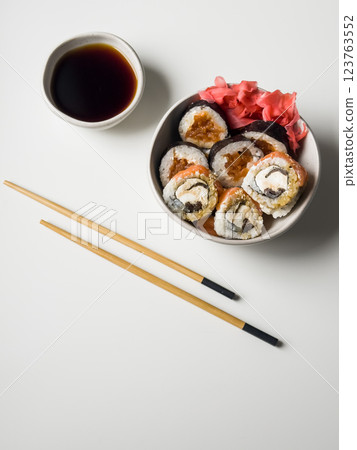 Sushi rolls in a bowl with pink ginger and soy sauce and wooden sticks on white table 123763552