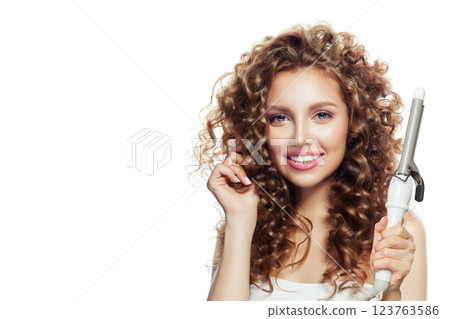 Excited brown haired woman with shiny long curly hairstyle showing curling iron. Excited brown haired woman with shiny long curly hairstyle showing curling iron. 123763586