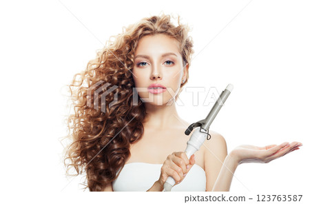 Pretty woman with healthy long wavy hair holding empty palm hand and using curlyng iron Pretty woman with healthy long wavy hair holding empty palm hand and using curlyng iron 123763587