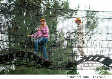 Adventure Park Rope Bridge Challenge Two people walk across a rope bridge in an adventure park. 123763892