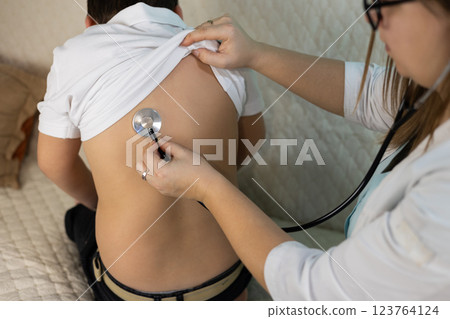 A pediatrician uses a stethoscope to examine the lungs of a sick child during a medical home visit. The pediatrician checks for respiratory illnesses or other health problems in the cute child. 123764124