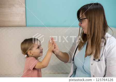 A smiling pediatrician gives a high five to her cute baby after a successful checkup during a home visit creating a trusting relationship between the doctor and the patient Doctor-child relationship. A smiling pediatrician gives a high five to her cute baby after a successful checkup during a home visit creating a trusting relationship between the doctor and the patient Doctor-child relationship. 123764126