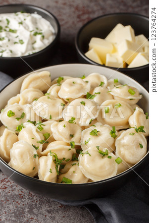 Hot boiled Russian pelmeni served with sour cream, butter and herbs close-up. Vertical 123764274