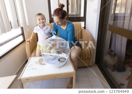 Mother and son caring for pet budgie in balcony with cat watching Mother and son caring for pet budgie in balcony with cat watching 123764949