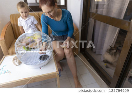 Mother and son feeding a parrot in a cage on the balcony Mother and son feeding a parrot in a cage on the balcony 123764999