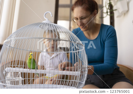 Mother and son observing a parrot in a cage at home Mother and son observing a parrot in a cage at home 123765001