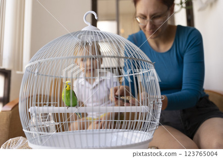 Mother and child feeding a green budgie in a cage Mother and child feeding a green budgie in a cage 123765004