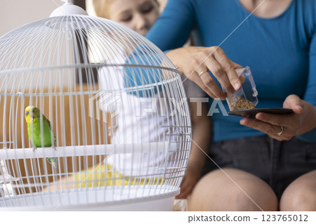 Mother and daughter feeding a green budgie in a cage 123765012
