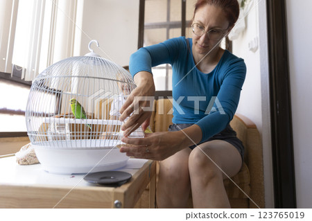 Woman changing water in a bird cage with a green parrot 123765019