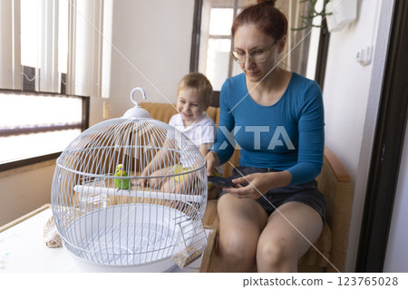 Mother and son admiring a green budgie in a white cage Mother and son admiring a green budgie in a white cage 123765028