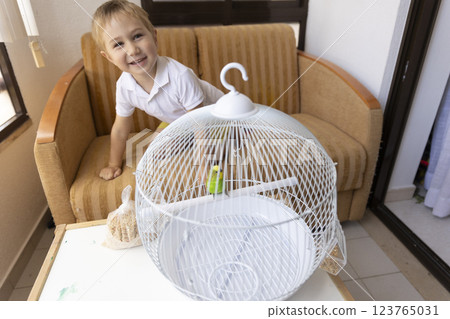 Smiling child playing with green parrot in white cage 123765031