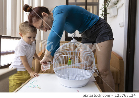 Mother and son changing water in bird cage at home 123765124