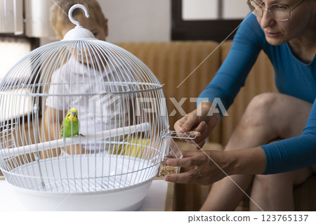 Woman replacing bird food in a cage while child watches 123765137