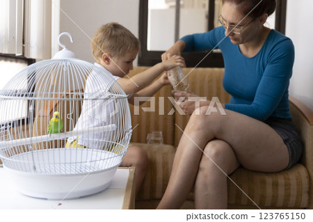 Mother and child feeding a parrot in a cage at home 123765150