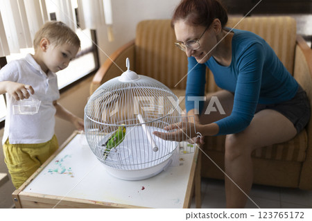 Mother and son caring for pet budgie in cage at home 123765172