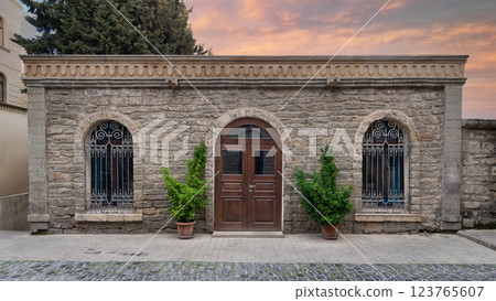 Rustic Stone Building With Wooden Door and Wrought Iron Window in an Urban Setting 123765607