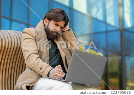 Indian young man using laptop browsing loses lottery results, bad news sitting in city street Indian young man using laptop browsing loses lottery results, bad news sitting in city street 123765626