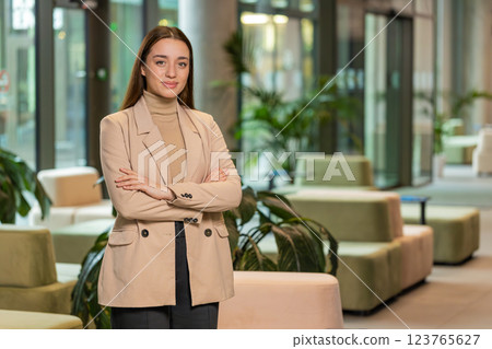 Portrait of happy young businesswoman with arms crossed looking at camera in office hotel lobby Portrait of happy young businesswoman with arms crossed looking at camera in office hotel lobby 123765627
