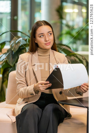 Caucasian young female entrepreneur in formal analyzing graph documents reports in office lobby Caucasian young female entrepreneur in formal analyzing graph documents reports in office lobby 123765628