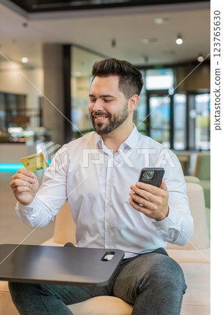 Happy businessman using credit card and smartphone for online shopping payments in office lobby Happy businessman using credit card and smartphone for online shopping payments in office lobby 123765630