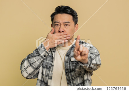 Frightened Asian man closing mouth with hands refusing to tell terrible secret, unbelievable truth 123765636