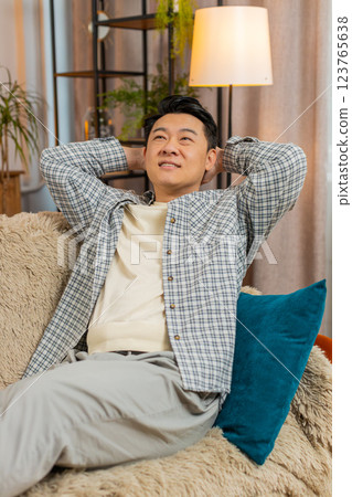Happy carefree middle-aged Chinese man sitting comfortably on sofa thinking in living room at home 123765638