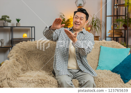 Cheerful rich Asian man showing wasting, throwing money around hand gesture sitting on sofa at home Cheerful rich Asian man showing wasting, throwing money around hand gesture sitting on sofa at home 123765639